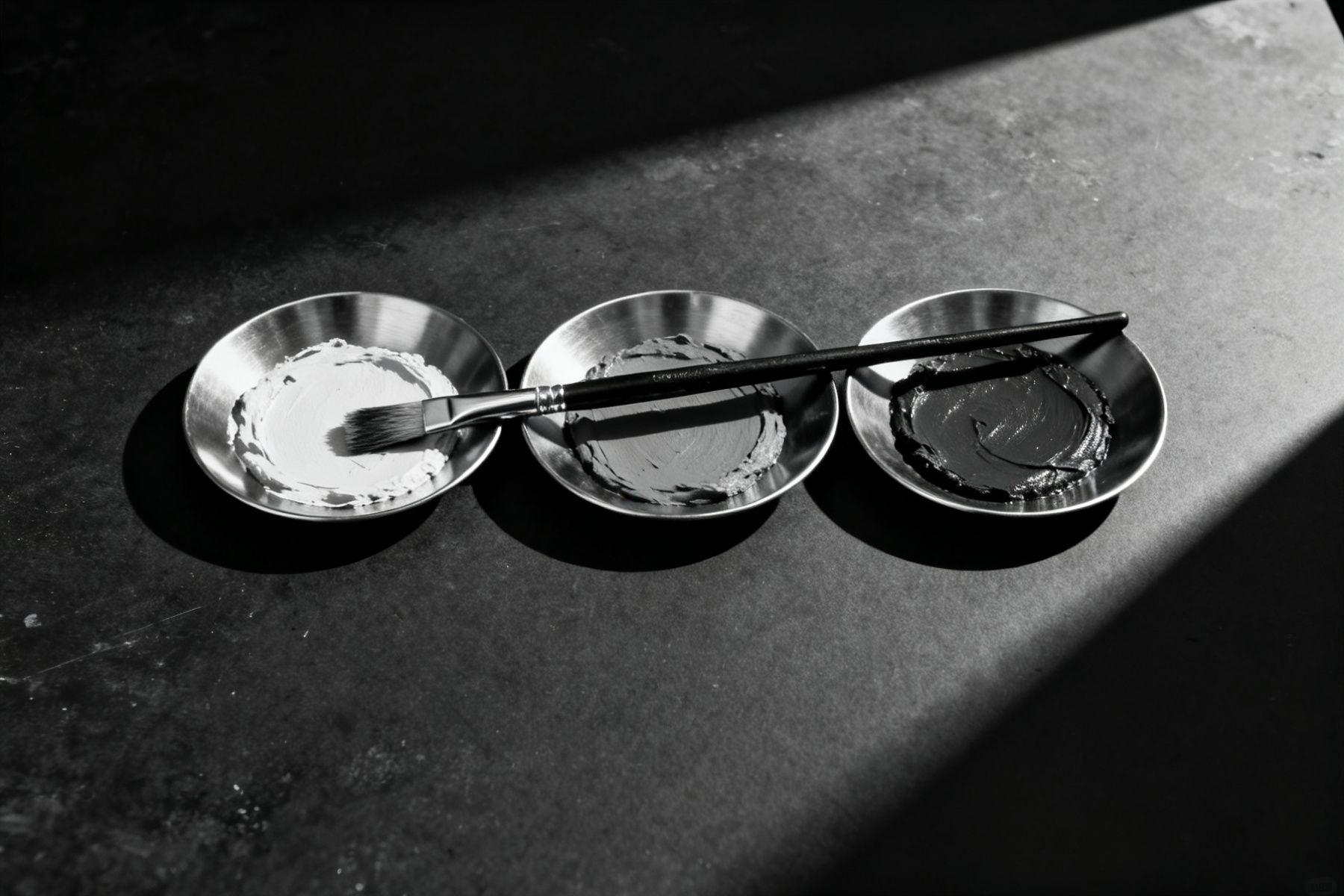 Mischschale mit heller Paste und ein Pinsel auf einer Metallfläche im Seitenlicht