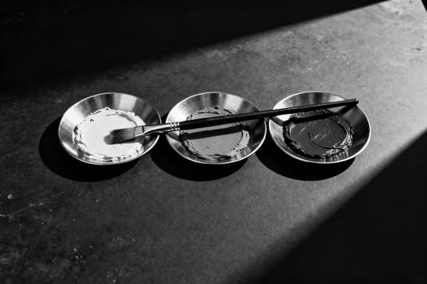 Mischschale mit heller Paste und ein Pinsel auf einer Metallfläche im Seitenlicht